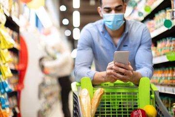 Wall Mural - Arabic Man Doing Grocery Shopping Using Smartphone In Supermarket