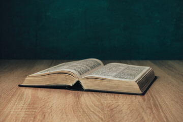 Wall Mural - Open holy bible on a  wooden table. Beautiful green wall background.