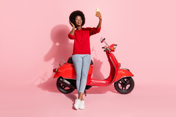 Poster - Full body portrait of cheerful dark skin lady hand touch hair make selfie sit on moped isolated on pink color background