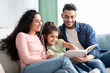 © Prostock-studio - Family Time. Happy Arab Mom, Dad And Little Daughter Reading Book Together