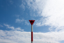 Red And White Pillar With A Red Triangular Sign And A Blue Cloudy Sky In The Background