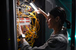 © Seventyfour - Side view portrait of female network engineer connecting cables in server cabinet while working with supercomputer in data center