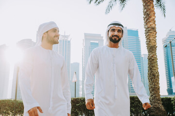 Wall Mural - Two young businessmen going out in Dubai. Friends wearing the kandura traditional male outfit walking in Marina