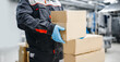 Factory industry worker holds a cardboard box in gloves against backdrop of production. Delivery distribution concept.