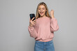 © dianagrytsku - Portrait of a young woman holding mobile phone and celebrating over gray background