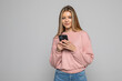 © dianagrytsku - Portrait of a cheery young woman using mobile phone while standing over gray background