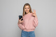 © dianagrytsku - Attractive woman showing ok gesture while holding blank screen mobile phone over gray background