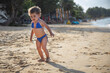 © Maria - happy little girl in a swimsuit runs along the beach with palm trees. adorable toddler girl in bikini on sandy beach of tropical ocean