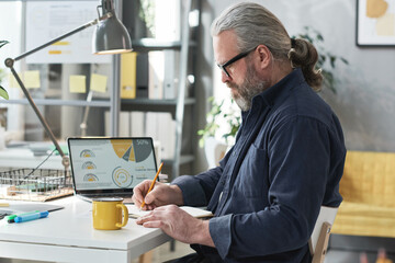 Wall Mural - Mature bearded businessman sitting at his workplace and working over new project at office