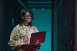 © Seventyfour - Waist up portrait of young African-American woman wearing military uniform using laptop while standing in server room, copy space