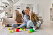 © insta_photos - Happy young family with kid playing enjoying time together at home in living room, parents with child sitting on floor near sofa, dad holding and kissing boy, mom smiling and feeling love.