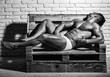 © Volodymyr - Muscular man with sexy muscle torso naked body in underpants on pallet sofa on white brick wall background.