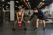 © etonastenka - Fitness couple in sportswear squatting with weights and doing squats in the gym. A personal trainer in the gym corrects the squats of a young athlete