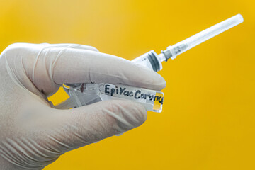 Ampoule with antiviral vaccine EpiVacCorona and medical disposable syringe. Injection drug in hand. Ampoule signed with black marker. Yellow background.