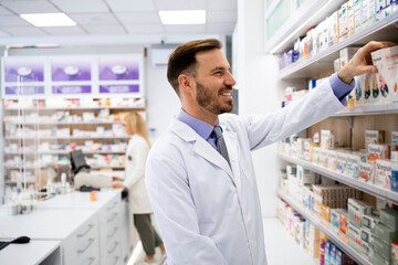 Wall Mural - Pharmacist working in pharmacy store and arranging boxes of medicines on the shelf.