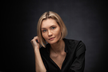 Beautiful middle-aged woman on a gray background in a black blouse.