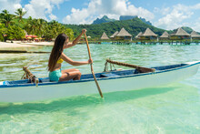 French Polynesia Tahiti Travel Vacation Concept. Outrigger Canoe Polynesian Watersport Sport Woman Paddling In Traditional Vaa Boat. Water Leisure Activity, Bora Bora Overwater Bungalow Resort Hotel