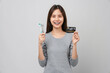 © sitthiphong - Smiling Asian woman wearing braces with tooth and holding toothbrush and dentist tool, credit card on grey background, Concept oral hygiene and health care.