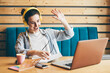 © Mariia Korneeva - Brunette lady with yellow earphones talks on video call at modern laptop sitting at wooden table near window in light co-working office close view.