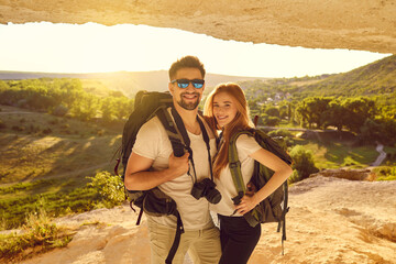Wall Mural - happy young couple of hikers standing in mountains cave at sunset. tourists mountaineering on summer