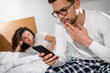 © Zoran Zeremski - Man using phone in bed while woman looking at him.