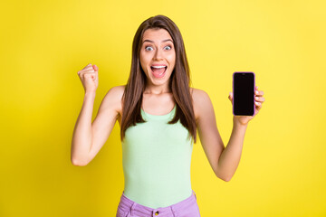 Canvas Print - Photo of crazy astonished lady show phone screen empty space raise fist wear green top isolated yellow color background