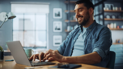 Wall Mural - Handsome Caucasian Man Working on Laptop Computer while Sitting on a Sofa Couch in Stylish Cozy Living Room. Freelancer Working From Home. Browsing Internet, Using Social Networks, Having Fun.