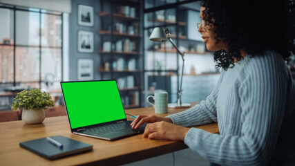 Wall Mural - Close Up Female Specialist Working on Laptop with Green Screen Mock Up Display at Home Living Room while Sitting at a Table. Freelancer Female Chatting Over the Internet on Social Networks.