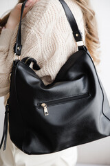 a rectangular black leather bag in the girl's hands. Indoors on a beige background