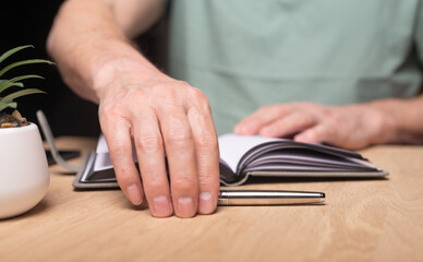 Poster - Male hands starting to plan his day, writing his schedule in organizer, diary, planner. Man taking pen at wooden desk.