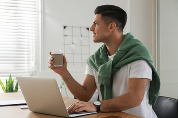 Wall Mural - Freelancer with cup of coffee working on laptop at table indoors