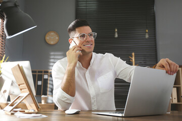 Wall Mural - Freelancer talking on phone while working at table indoors