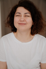 smiling with eyes closed brunette woman with curly hair in a white T-shirt. 