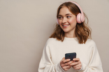 Wall Mural - Young smiling woman listening music with headphones and cellphone