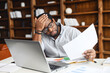 © Vadim Pastuh - Displeased African-American man looking through workpapers, stressed black male employee reading a document bank statement sitting in the office, has bad balance, bankruptcy, debt