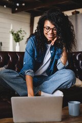 Vertical portrait of an african-american young girl working on laptop at home. Front view of smiling african female freelancer using laptop