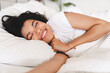 © InsideCreativeHouse - Happy sleepy african young woman lying in her bed in the morning before getting up. Cheerful young woman lying on bed playing with blanket and looking at camera.
