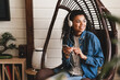 © InsideCreativeHouse - Young beautiful african-american woman listening to the music in the rocking chair in cosy flat. Pleased black girl chilling on chair on balcony, enjoying morning alone, having fun on terrace