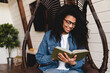 © InsideCreativeHouse - Smart african young woman reading a book in cosy armchair in modern house. People and leisure concept. Weekend Pastime.