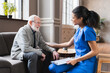 © InsideCreativeHouse - African nurse in uniform talking during day visit to old patient grandfather. Caring caregiver hold hand of 80s senior elderly man people having pleasant conversation.
