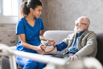 Woman doctor cardiologist or physician checking high blood pressure examining old male patient using tonometer during home medical care visit. Elderly hypertension cardiovascular problems concept.