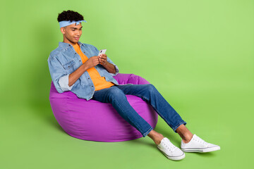 Poster - Full length body size photo of young guy in beanbag using cellphone app browsing internet isolated on vibrant green color background