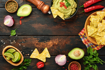 Guacamole. Traditional latinamerican Mexican dip sauce in a black bowl with avocado and ingredients and corn nachos. Avocado spread. Top view. Copyspace