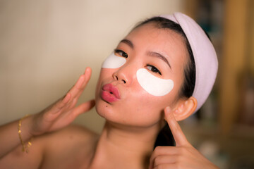 portrait of young happy and beautiful asian korean woman applying facial anti panda eyes patch at ba