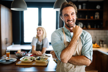 Wall Mural - Beautiful young couple is smiling while cooking together in kitchen at home