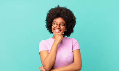 Wall Mural - afro black woman smiling with a happy, confident expression with hand on chin, wondering and looking to the side