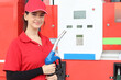 © Stella - Portrait of happy smiling beautiful woman gas station attendant in red uniform holding a fuel petrol pump nozzle against at gas station.