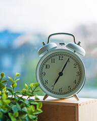 The white vintage alarm clock showing time 7 am in the morning next to the window under morning light.