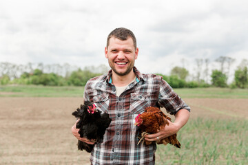 a young male farmer with a chicken in his hands stands in his garden in the village.