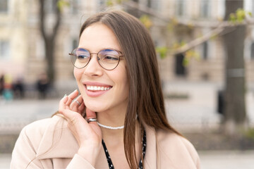 Portrait of a joyful woman wearing glasses with a perfect smile looking on the side outdoors in the city park 